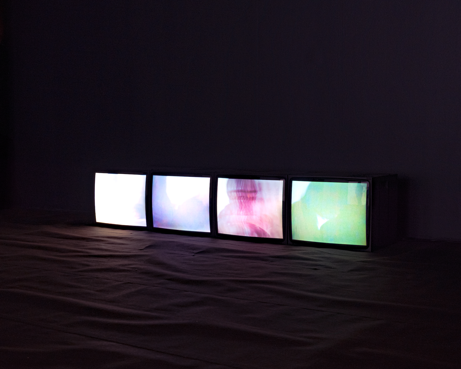 Four glowing monitors displaying colorful abstract images lined up on a dark floor.