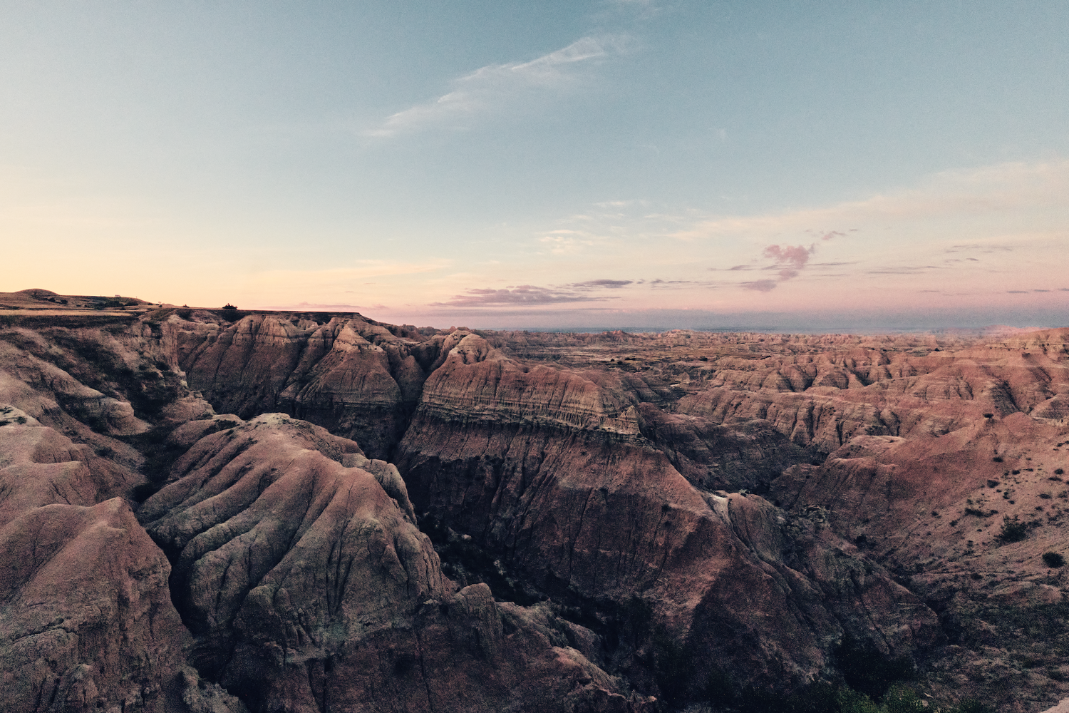 Panoramic sunset view of rugged badlands canyon landscape with colorful sky.
