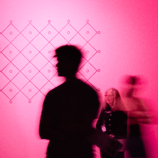Silhouetted figures cast pink shadows against a magenta wall with geometric diamond pattern artwork.