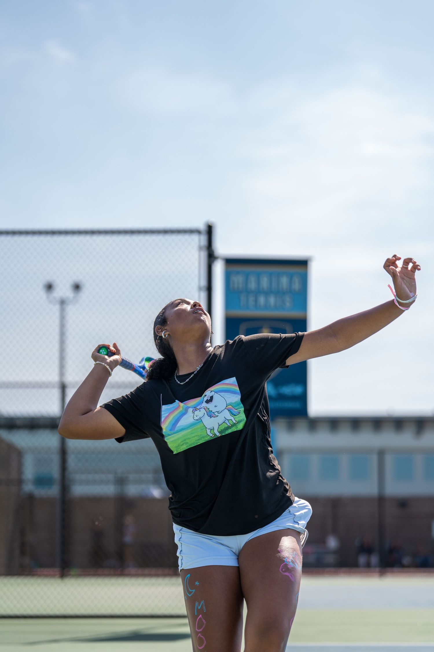 Female tennis player in black t-shirt tossing ball upward preparing to serve outdoors.