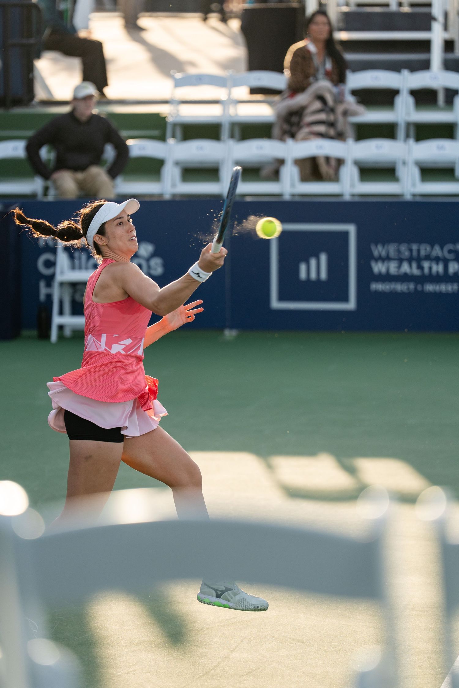 Female tennis player in pink hits backhand at evening Westpac Wealth tennis tournament.