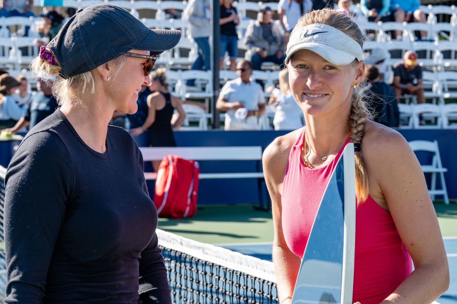 Two women chat at tennis net during San Diego Open WTA tournament on sunny day.