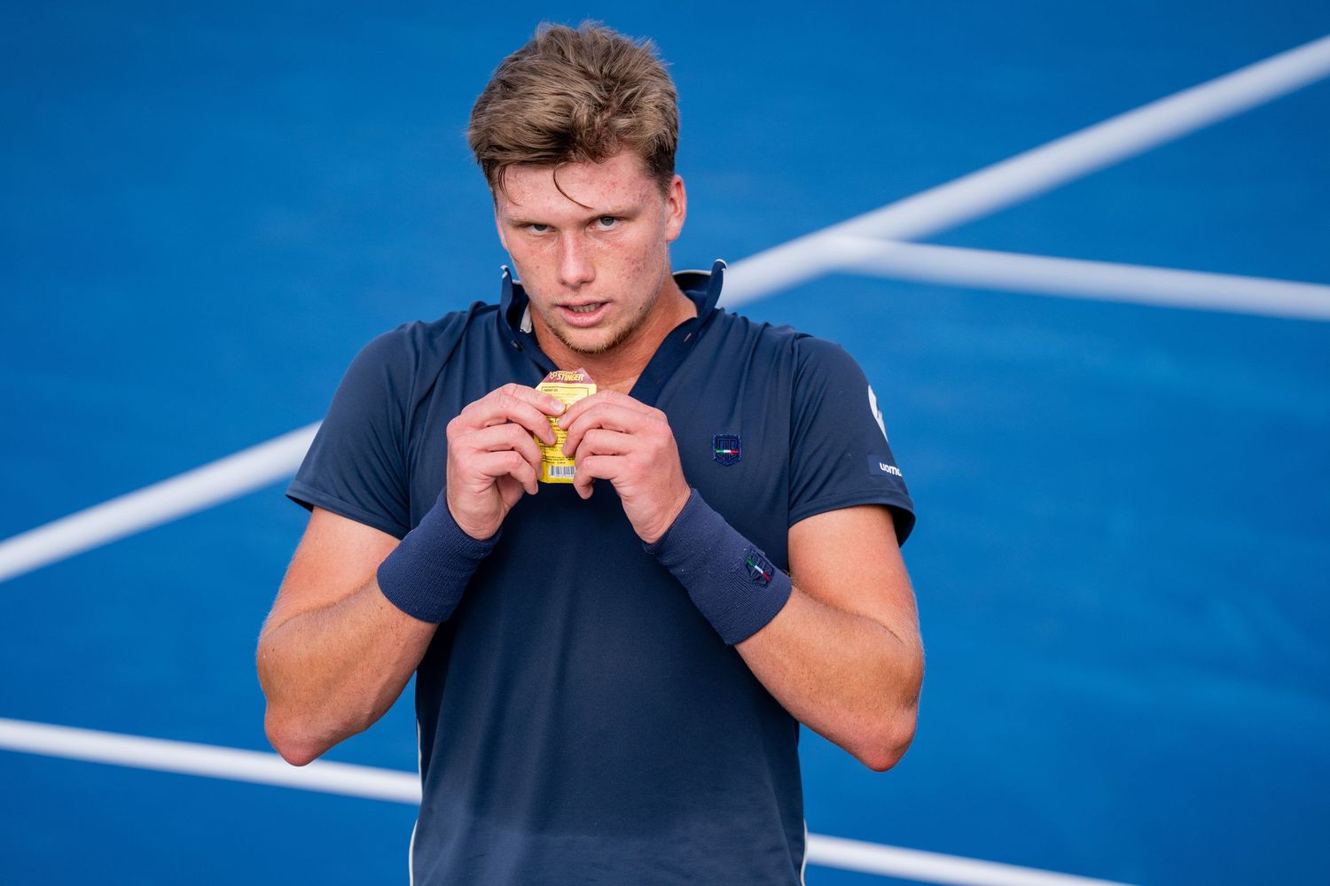 Young male tennis player examines tennis ball on blue hard court.