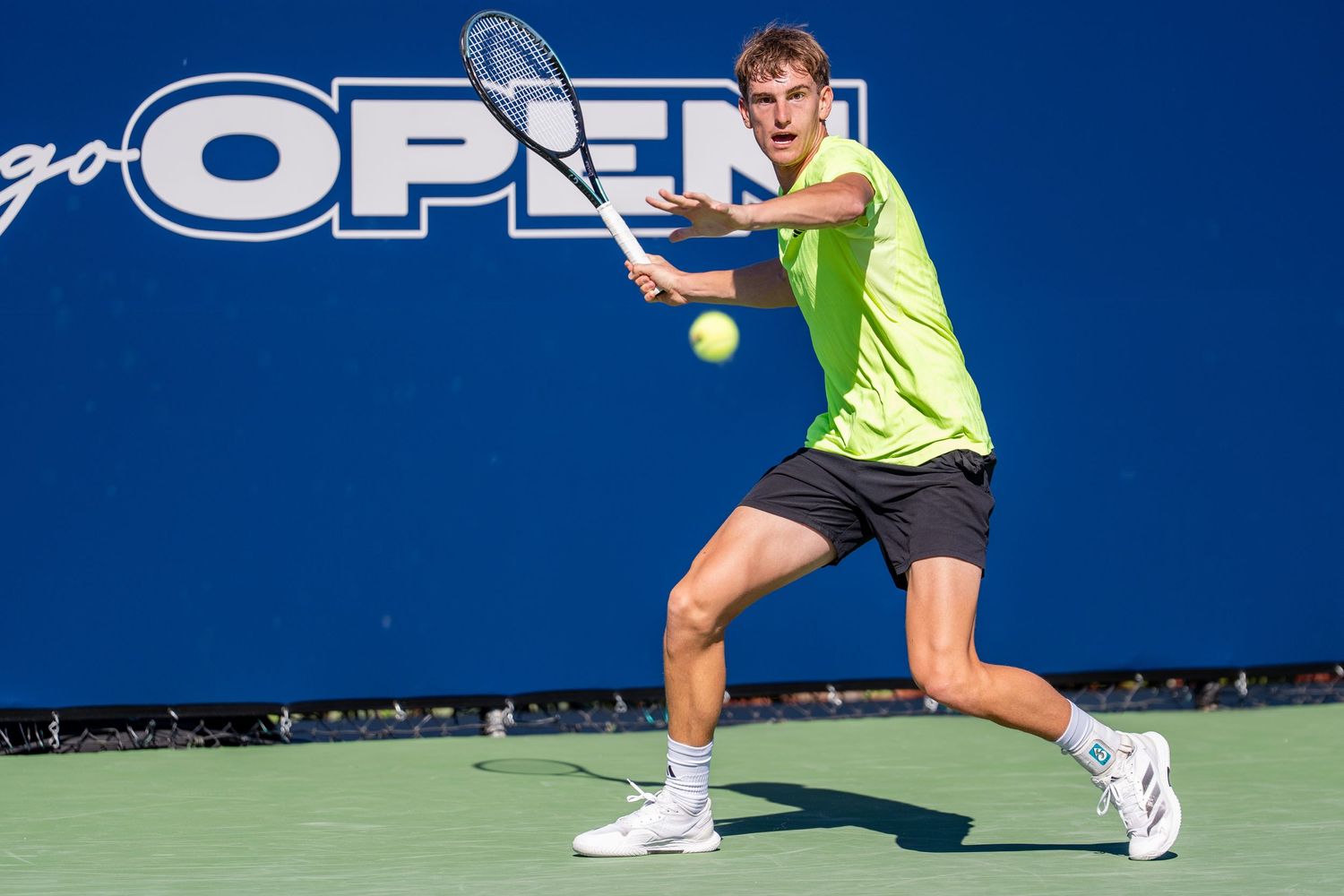 Male tennis player in yellow shirt hitting a backhand shot at the San Diego Open tennis tournament.
