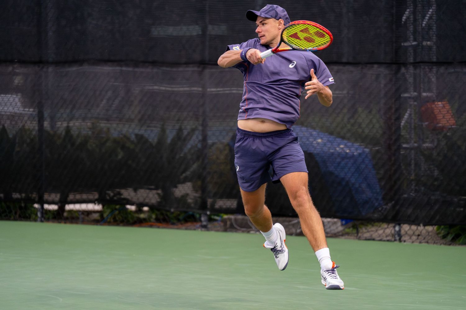 Tennis player in navy outfit jumps to hit a powerful forehand shot on an outdoor tennis court.