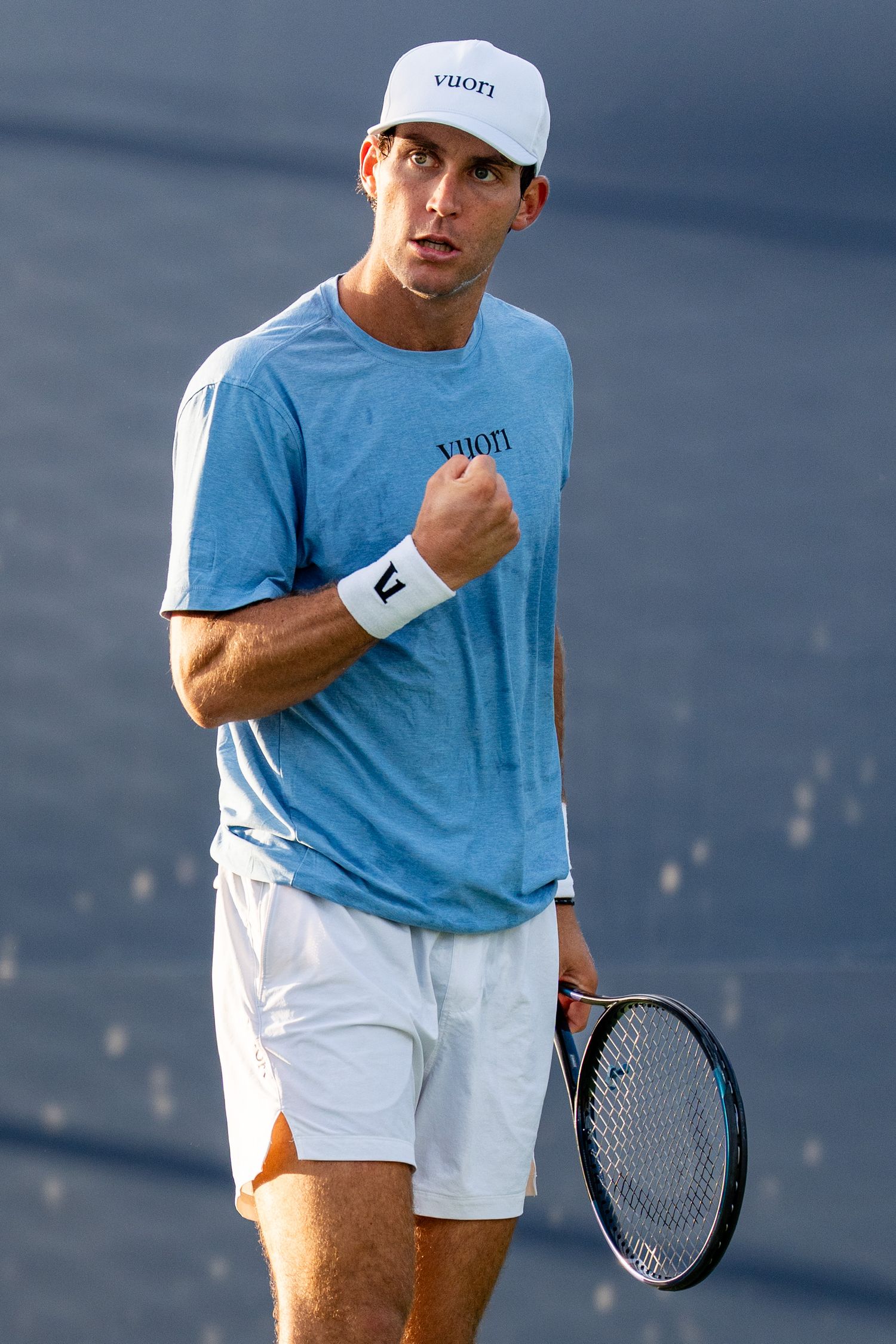 Male tennis player in Vuori blue shirt pumps fist celebrating point on court.