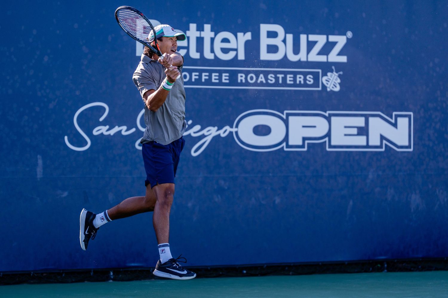 Male tennis player follows through on a backhand shot at the Better Buzz Coffee Roasters San Diego Open.