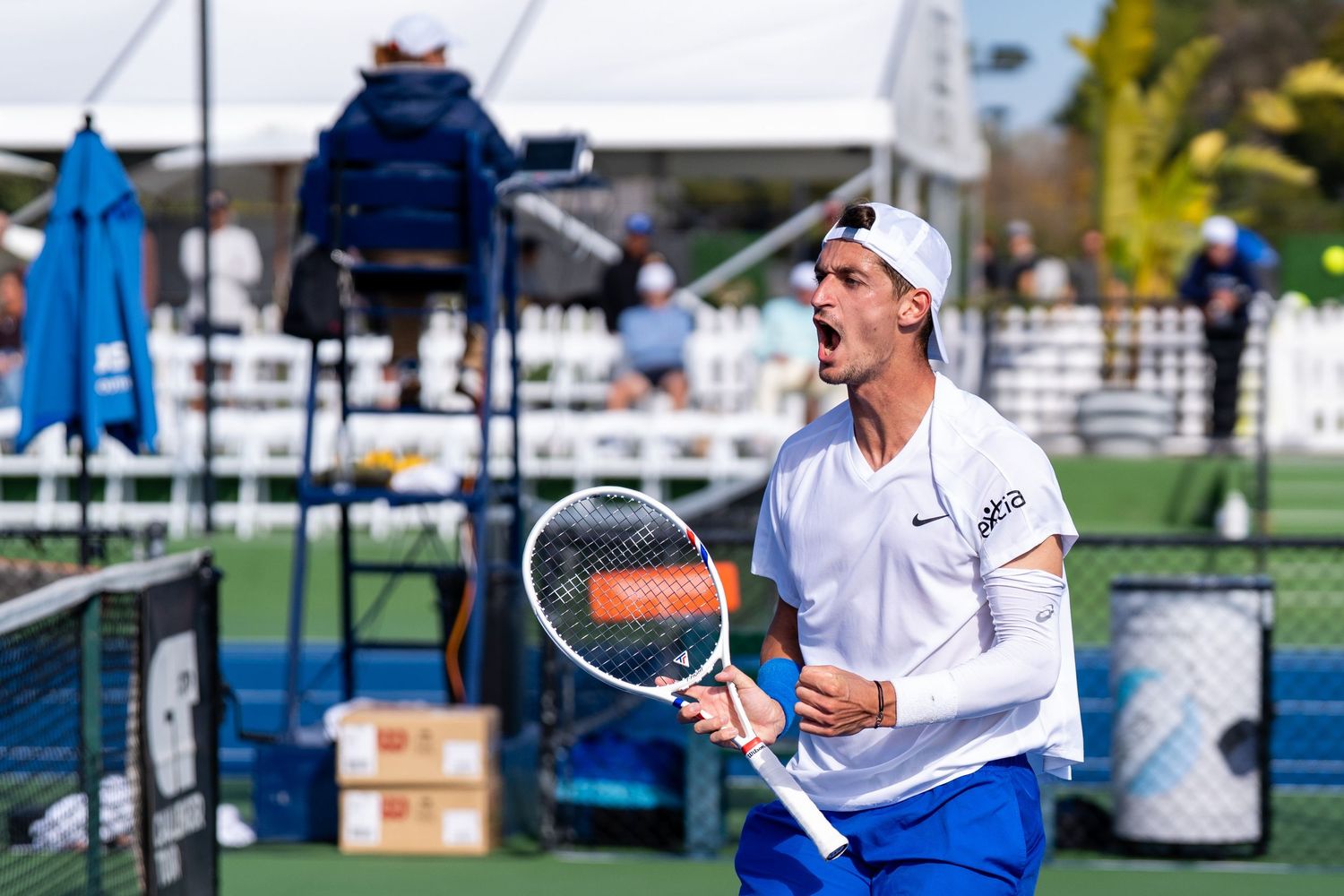 Male tennis player celebrates a point with an open-mouthed shout during an outdoor tournament match.
