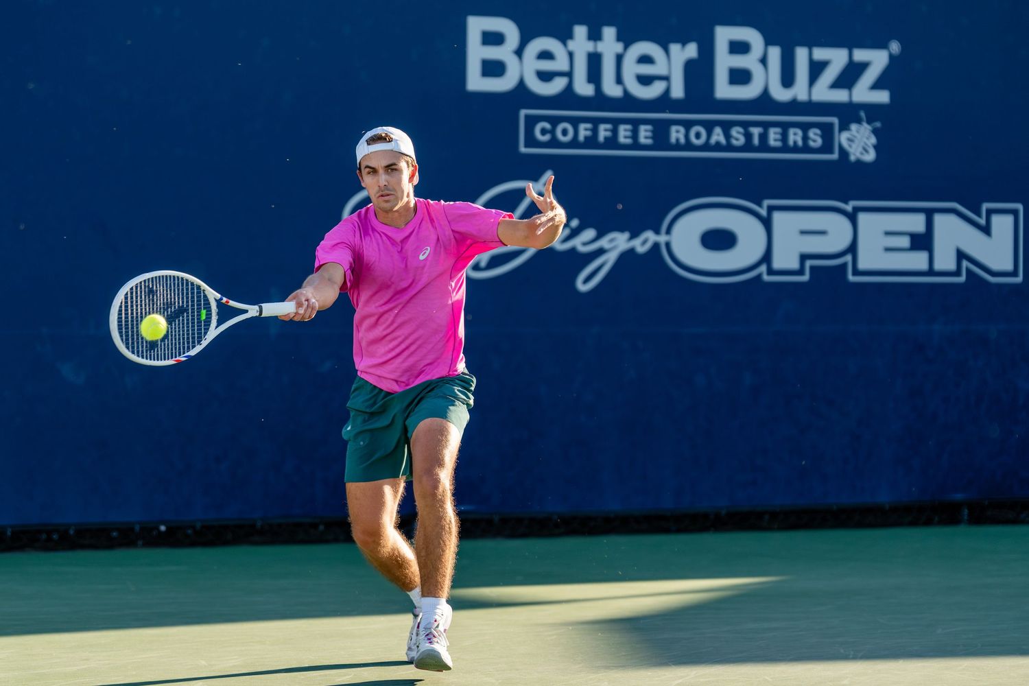 Male tennis player in pink shirt returns forehand at the Better Buzz Coffee Roasters San Diego Open tournament.