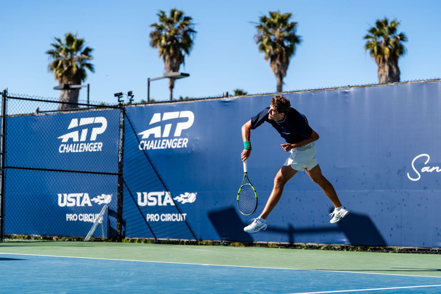 Male tennis player serving on blue court at ATP Challenger USTA Pro Circuit tournament.