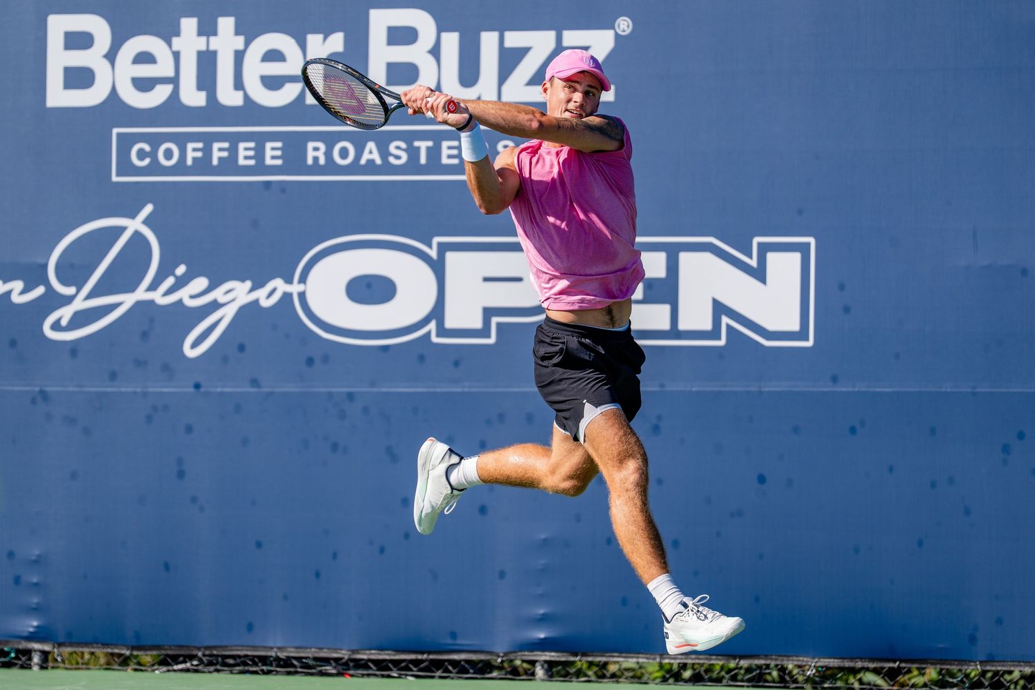 Male tennis player in pink shirt hitting forehand at Better Buzz Coffee Roasters San Diego Open.