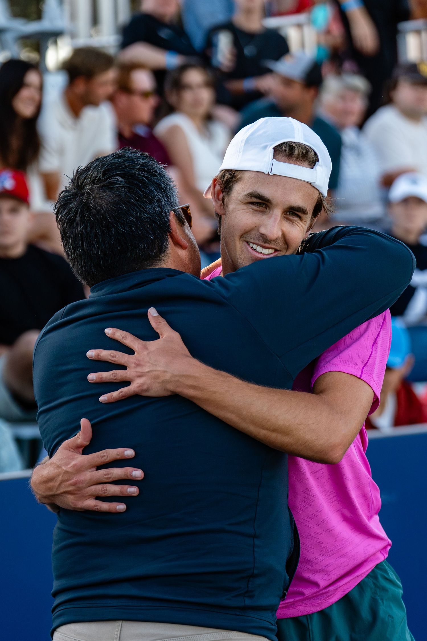 Smiling tennis player in pink hugs coach courtside after winning match at San Diego Open tournament.