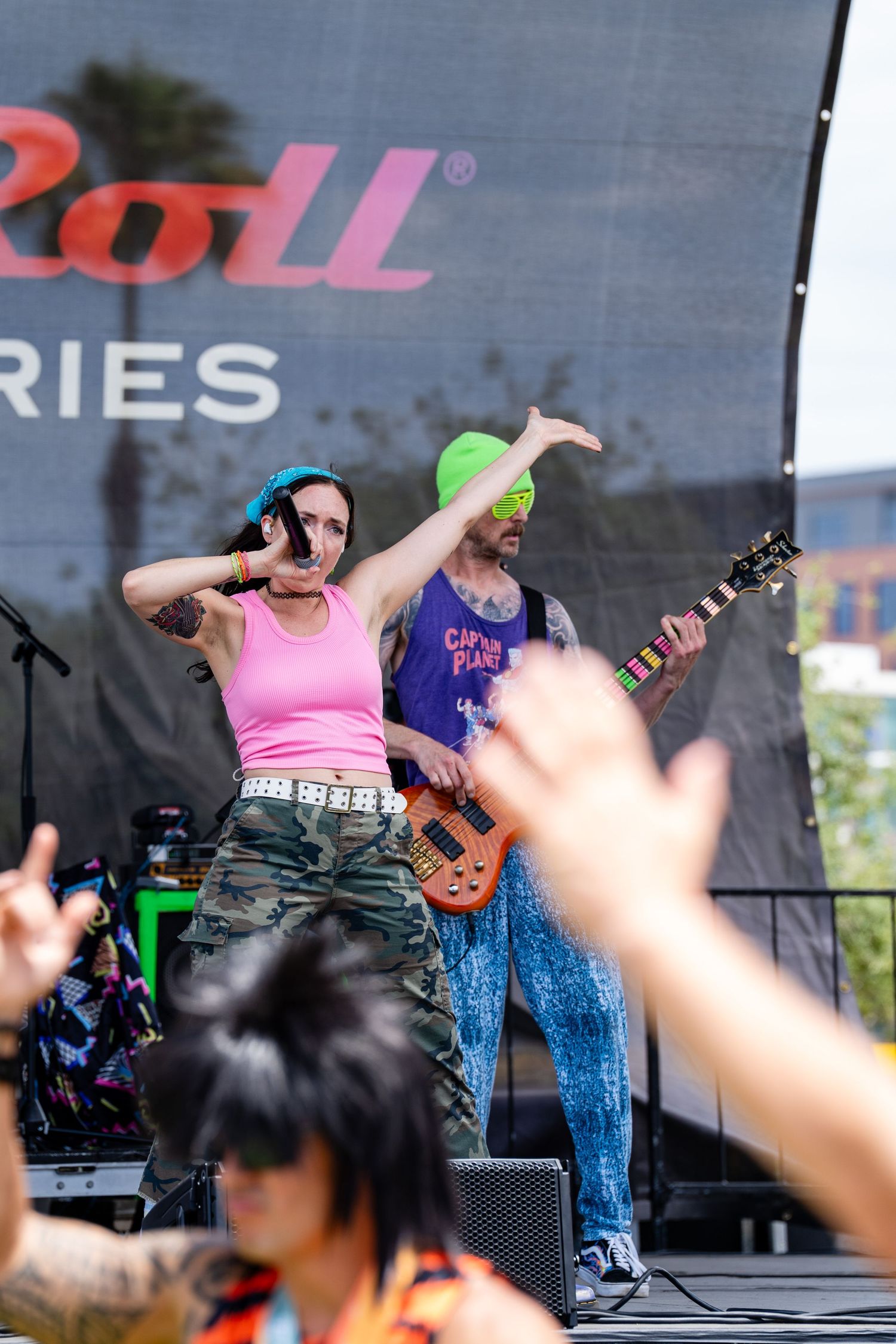 Female vocalist and green-masked guitarist perform energetically on stage at a Rock and Roll series event.
