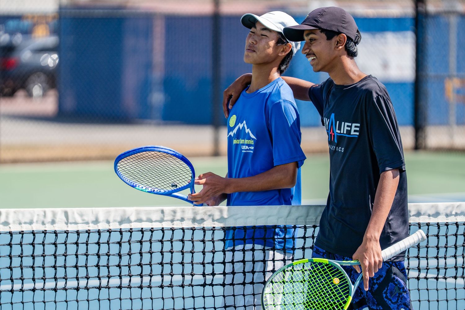 Two young tennis players shaking hands at the net after a match on an outdoor hard court.
