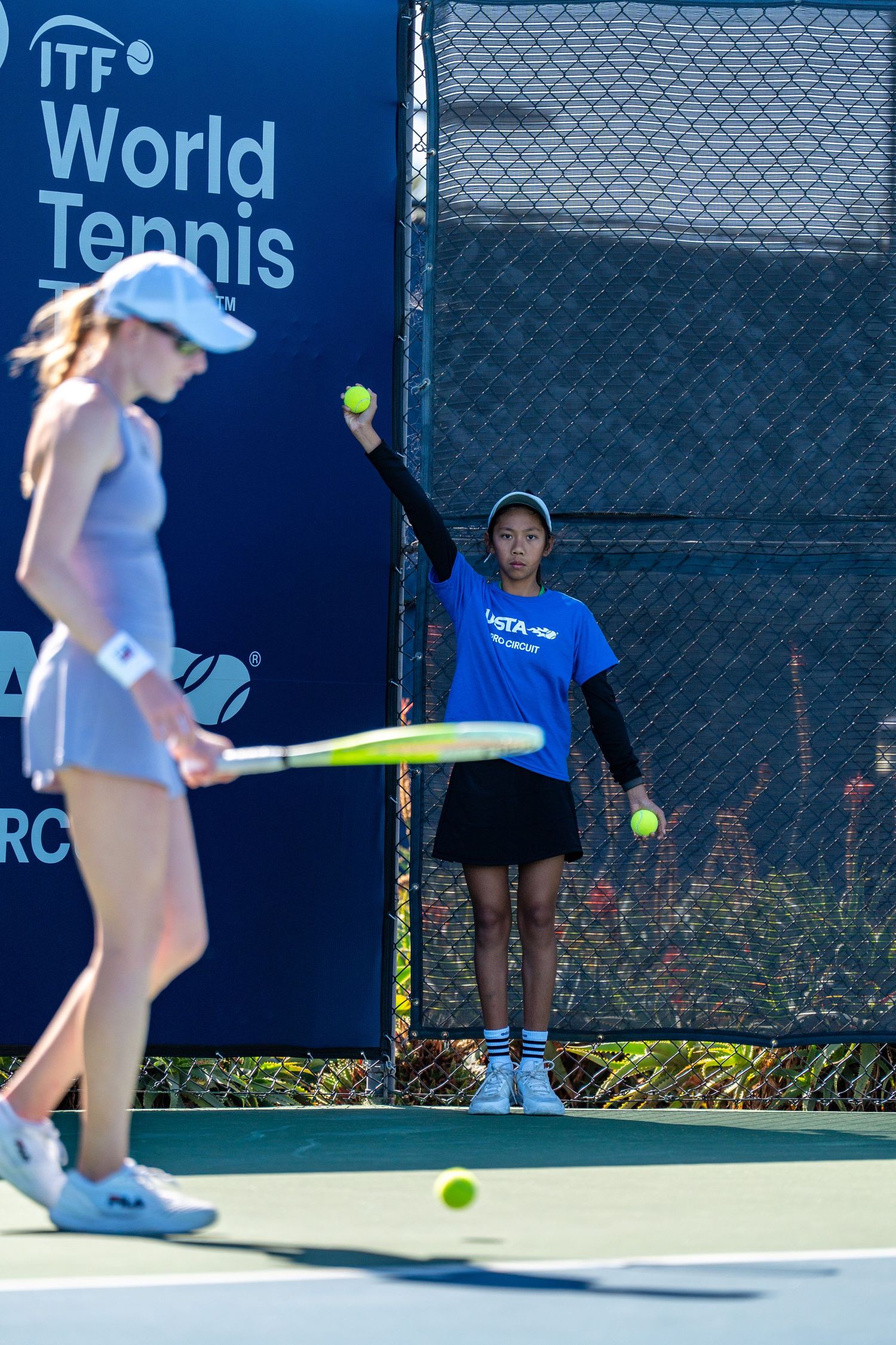 Ball girl raising tennis ball on court during ITF World Tennis tournament match.