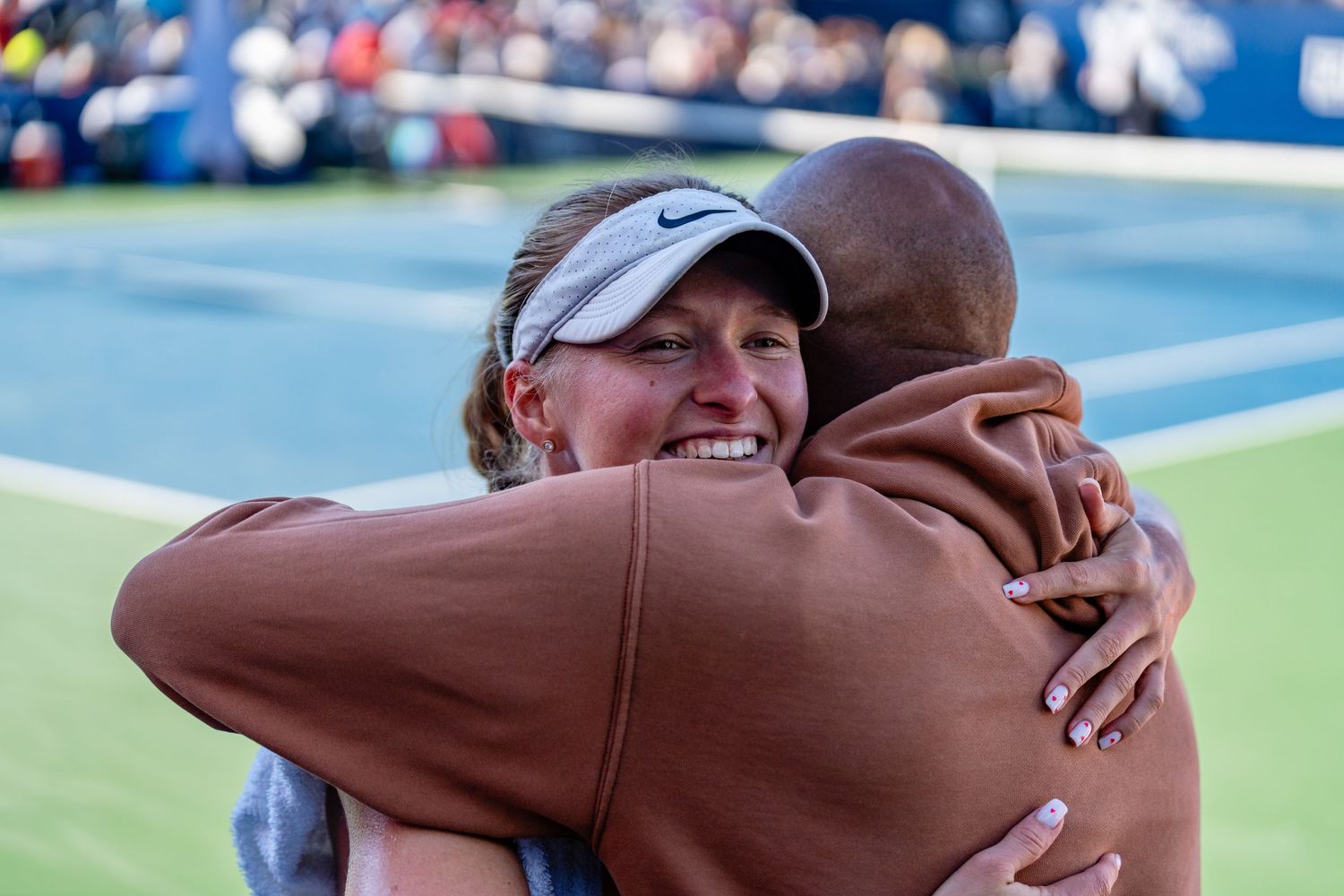Female tennis player smiling while embracing a coach or supporter after a match at a professional tennis event.