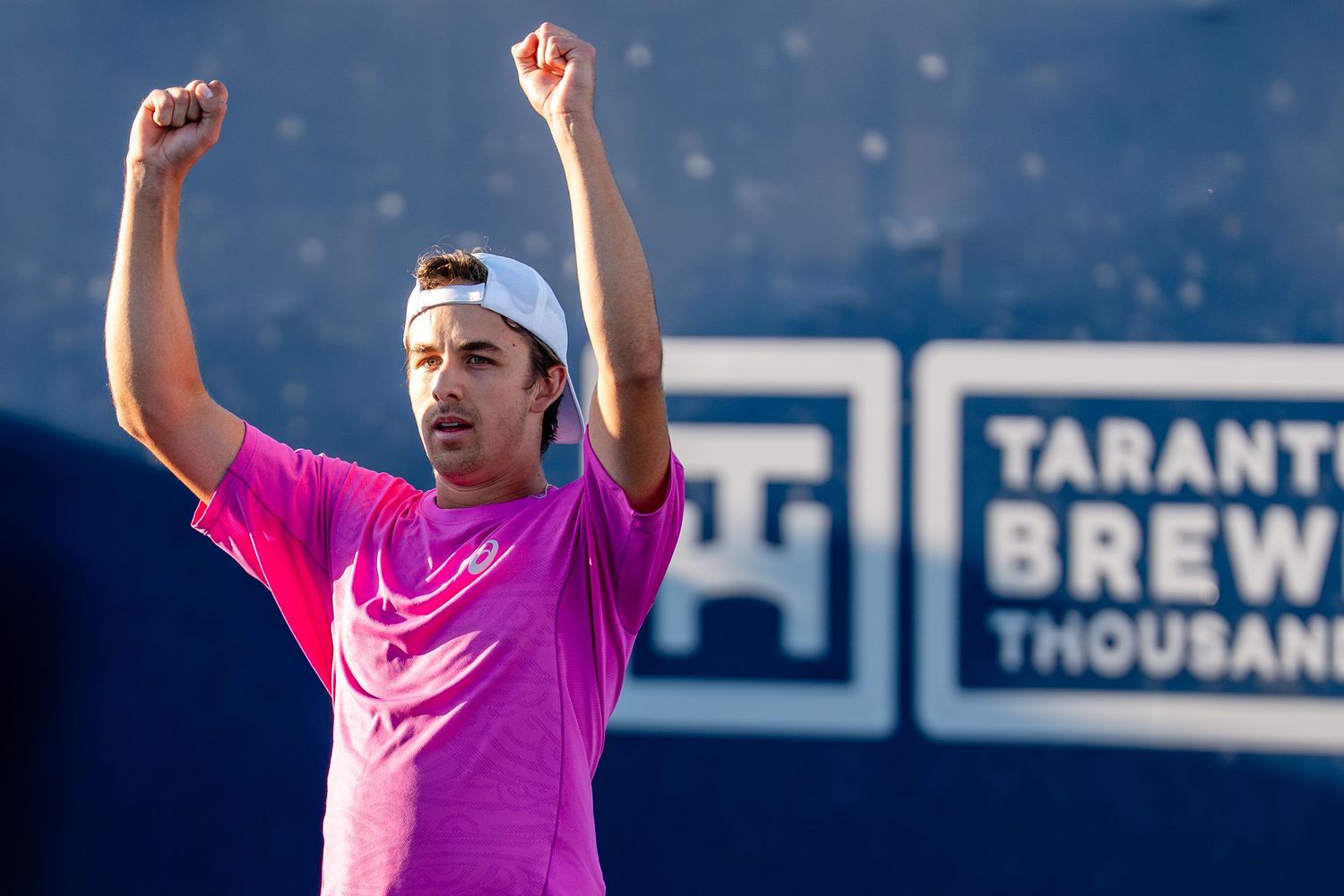 Jubilant tennis player in pink raises both fists in victory celebration at Taranto Brewery tournament.