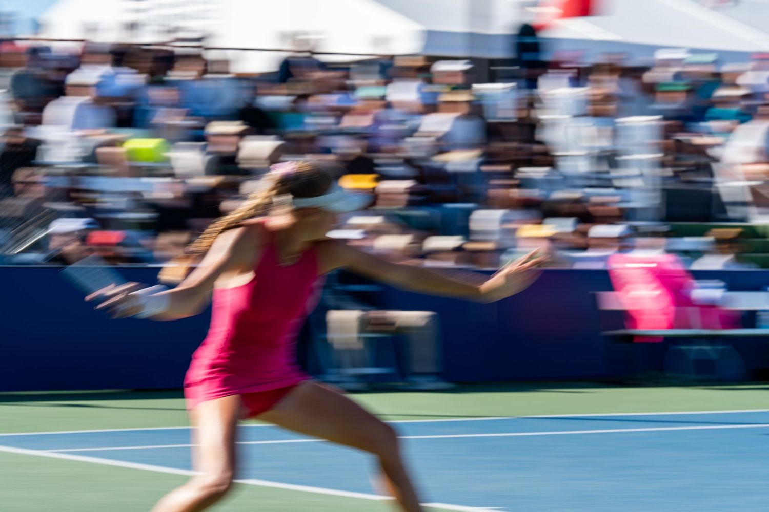 Motion blur action shot of a female tennis player in pink dress running during a professional tennis match.