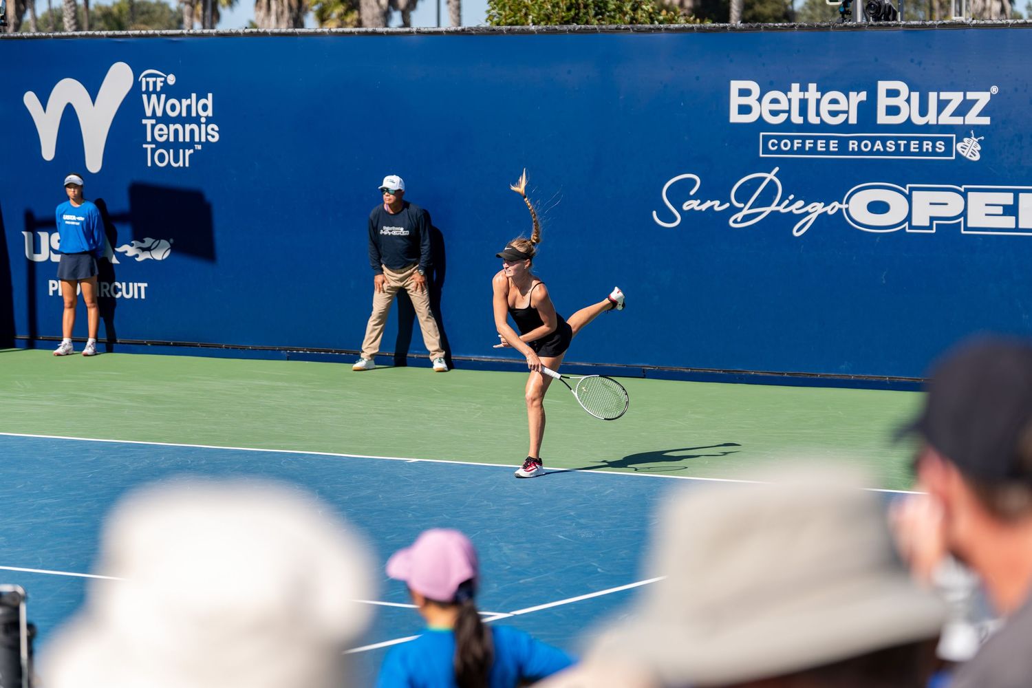 Female tennis player serves at the San Diego Open on the WTA World Tennis Tour on a sunny day.