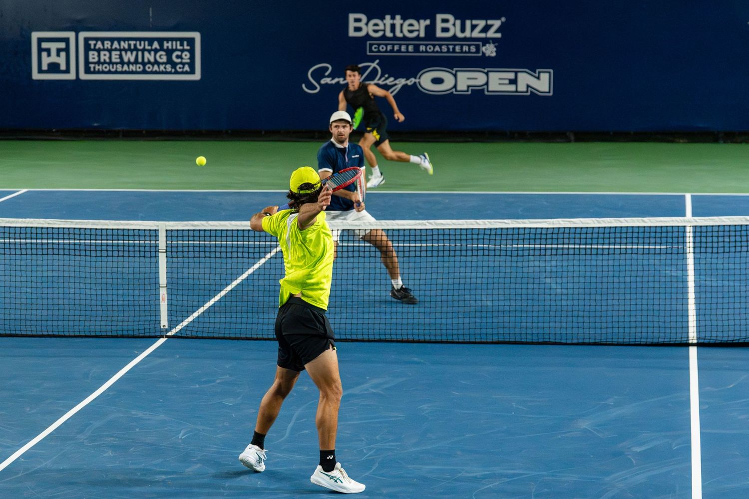 Doubles tennis team in action at the Better Buzz Coffee Roasters San Diego Open at night.