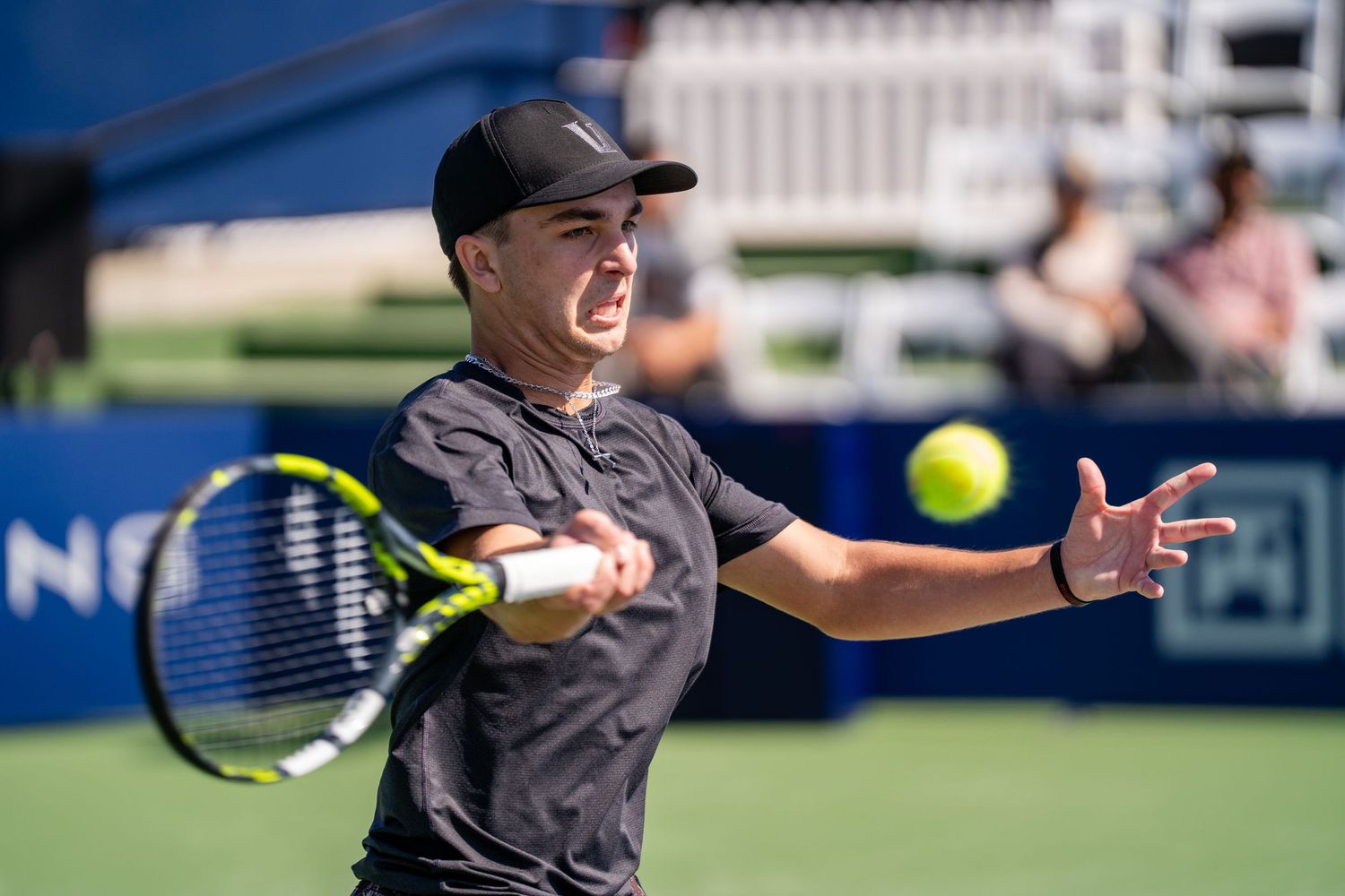 Tennis player in black cap and shirt hitting forehand on outdoor blue hard court.