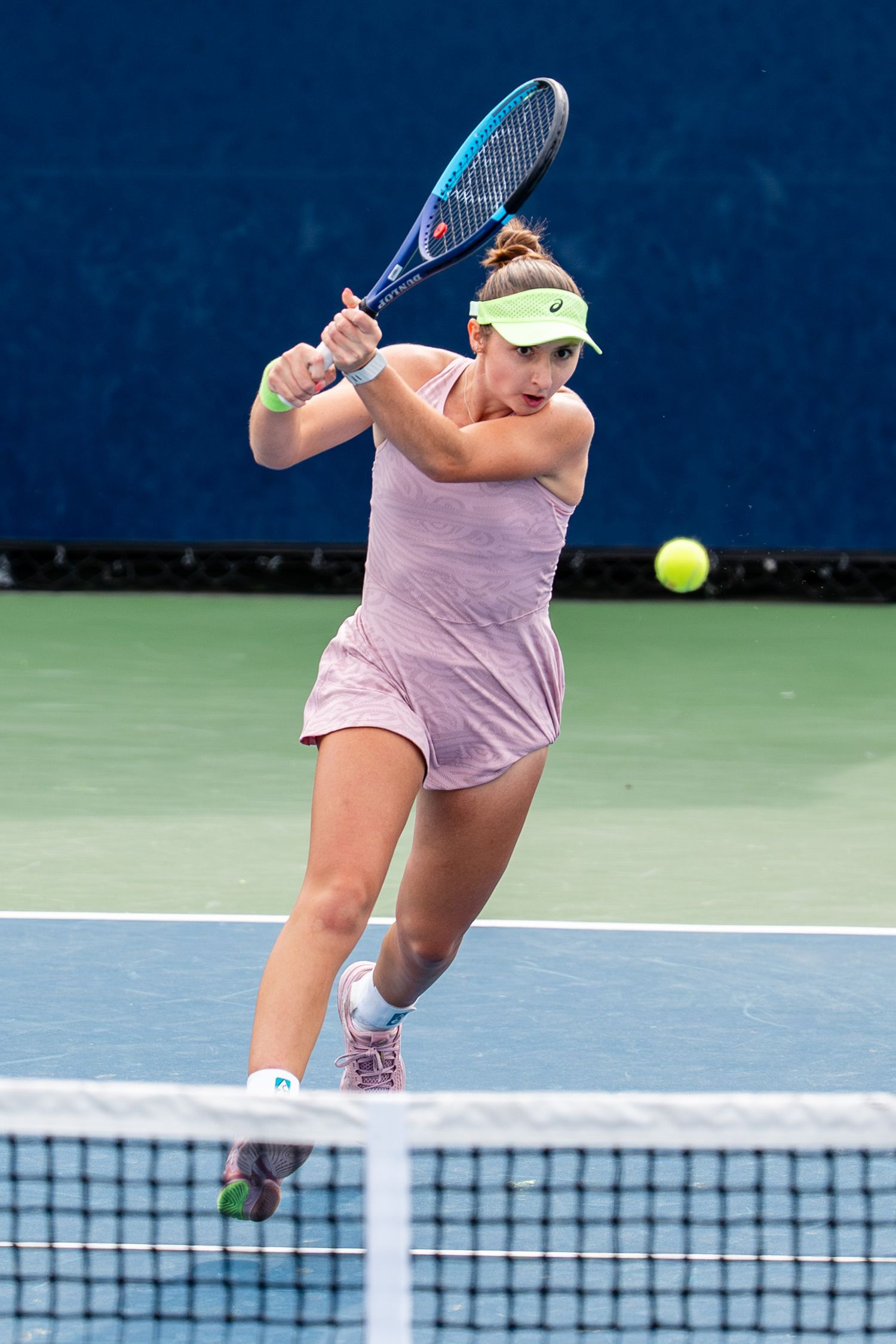 Female tennis player in pink outfit hitting a backhand shot on a blue hard court.