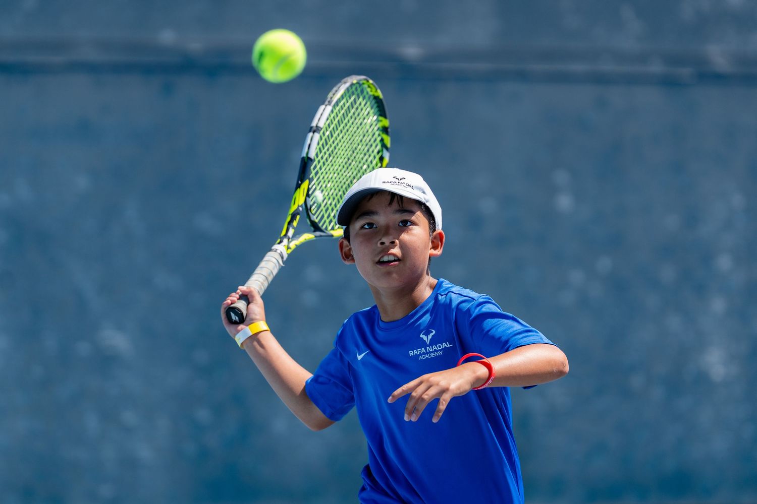Young boy in blue shirt hitting a tennis ball with a racket on an outdoor court.