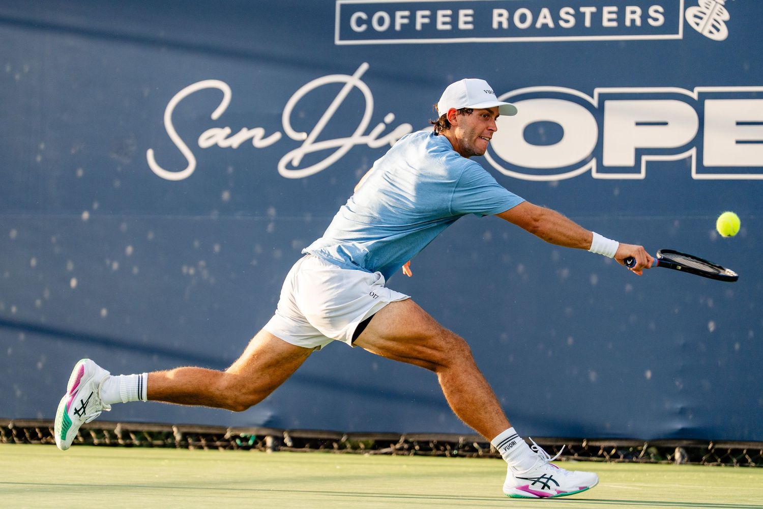 Tennis player lunges to hit a low backhand shot at the San Diego Open Coffee Roasters tournament.
