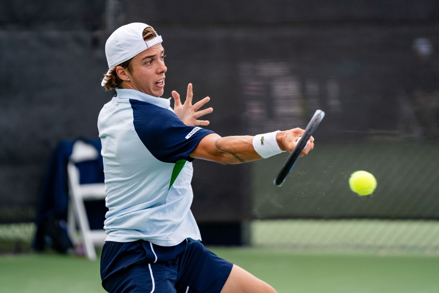 Tennis player in navy outfit hits forehand volley on outdoor court.