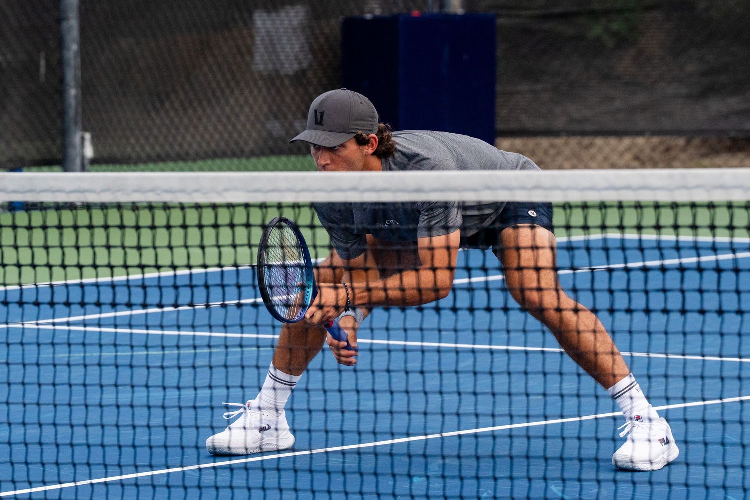 Tennis player crouches low near the net preparing to return a shot on a blue court.