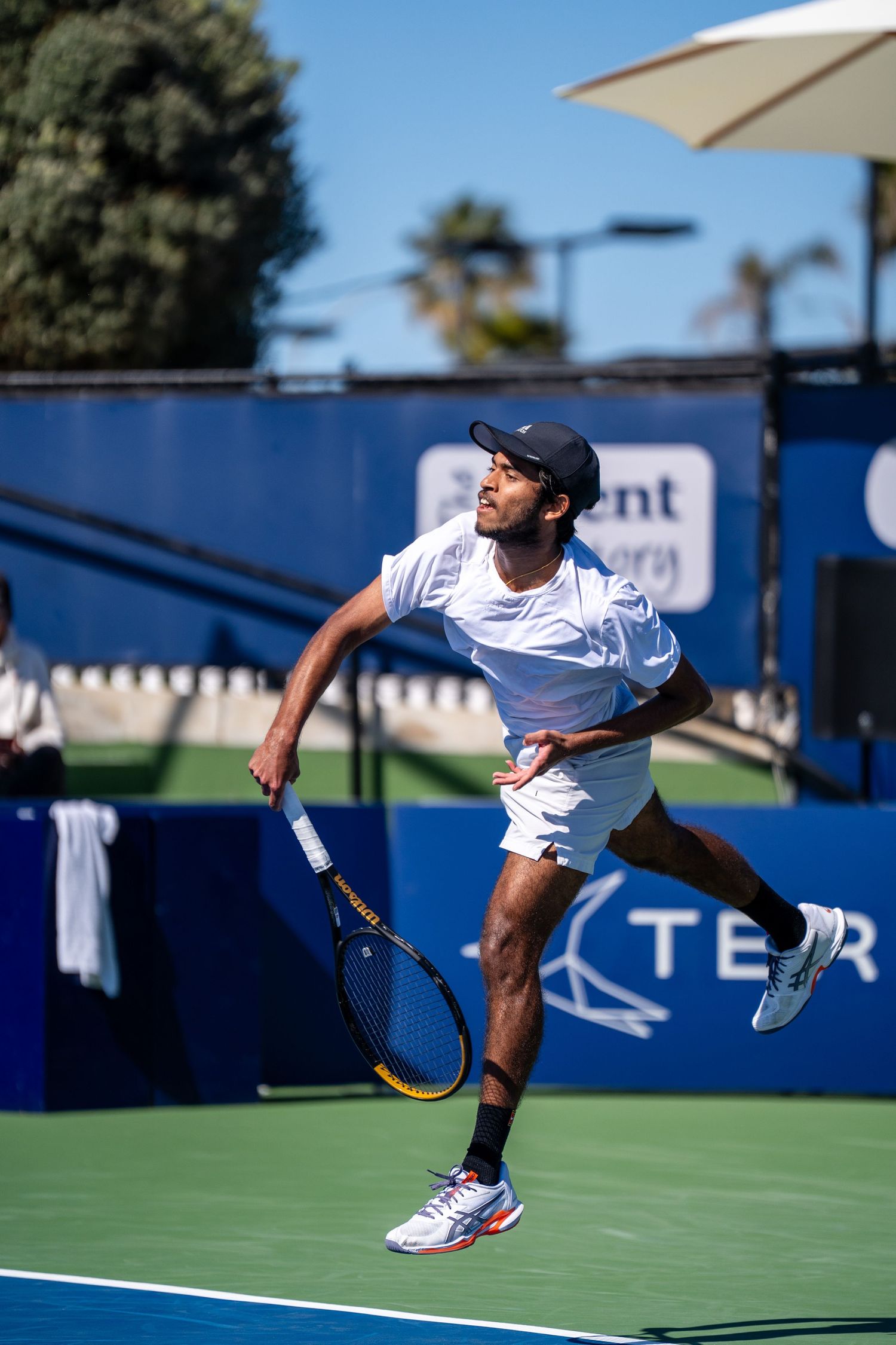 Male tennis player serves the ball on an outdoor hard court during a sunny professional match.