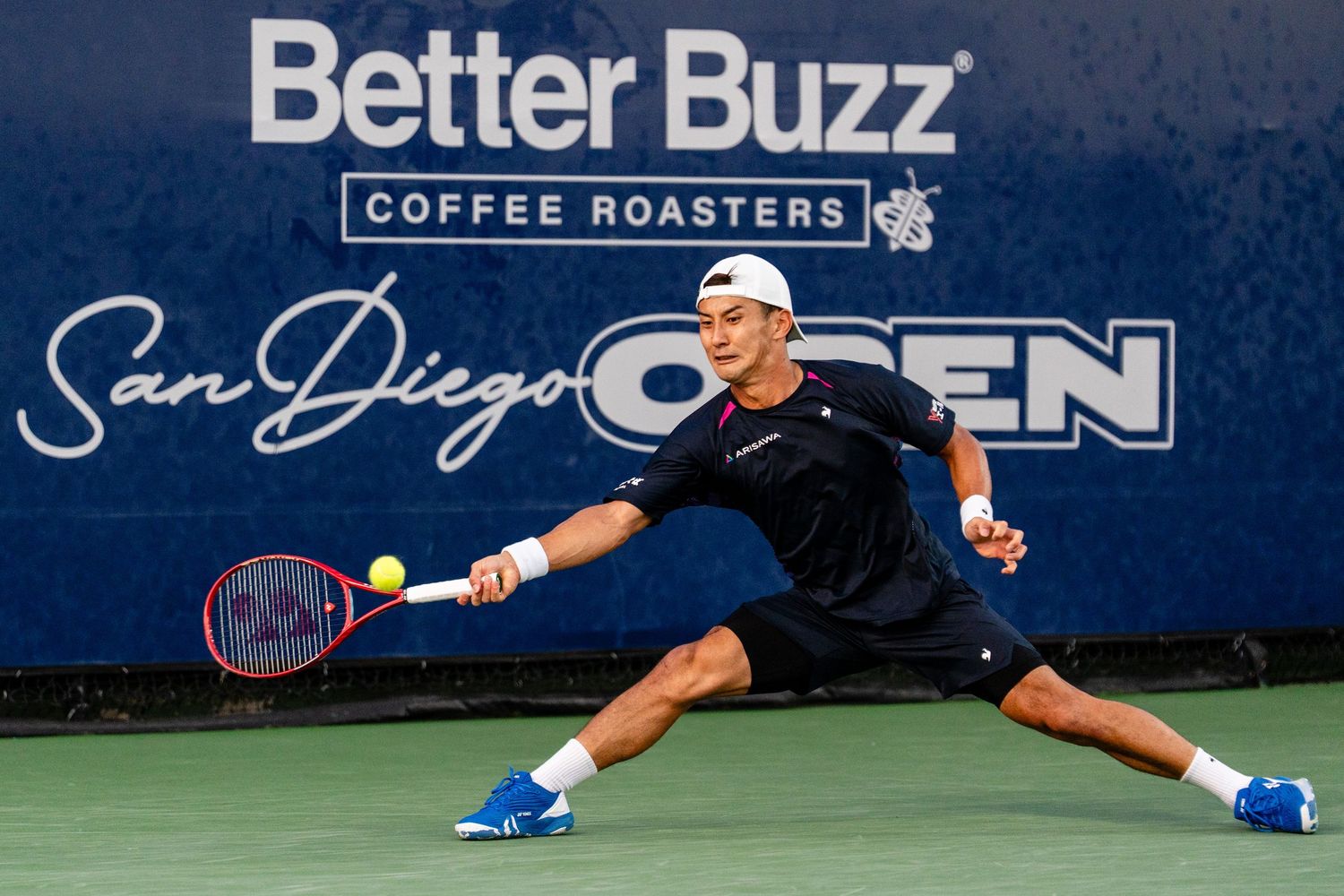 Tennis player lunges for a forehand shot at the San Diego Open, sponsored by Better Buzz Coffee Roasters.