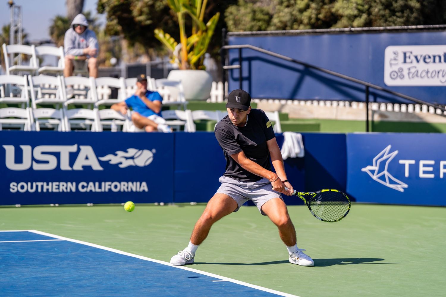 Male tennis player hits a low backhand shot on a USTA Southern California outdoor court.