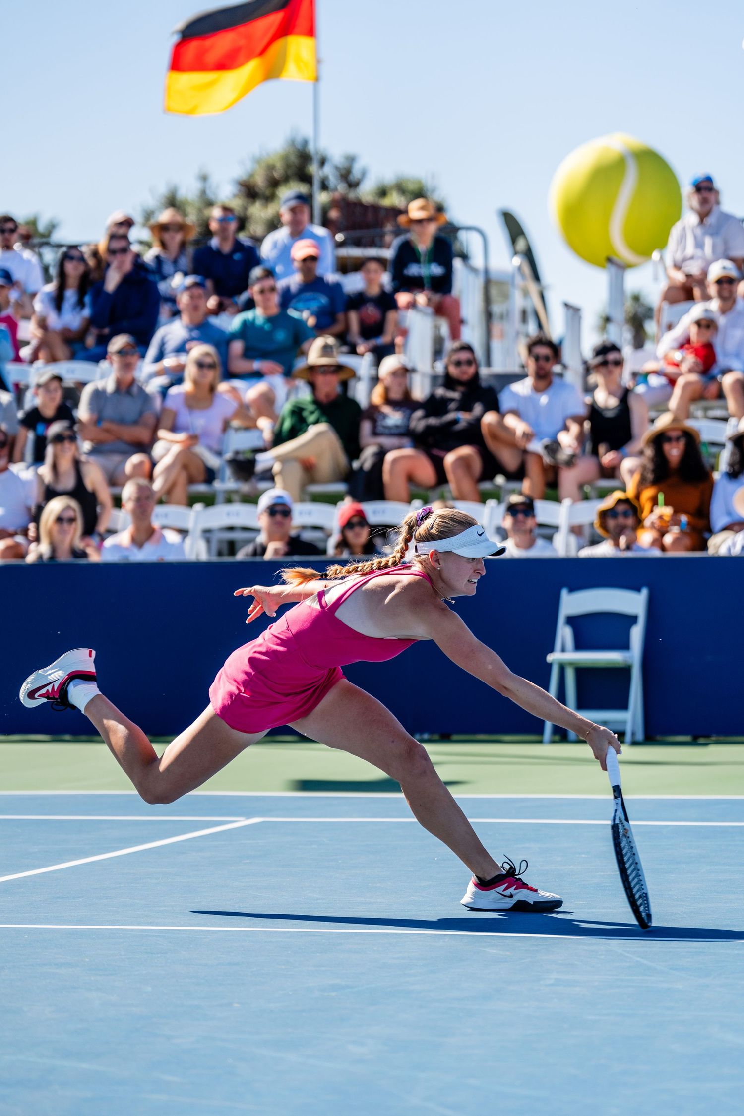 Female tennis player in pink stretches for a low forehand shot before a packed crowd at the San Diego Open.