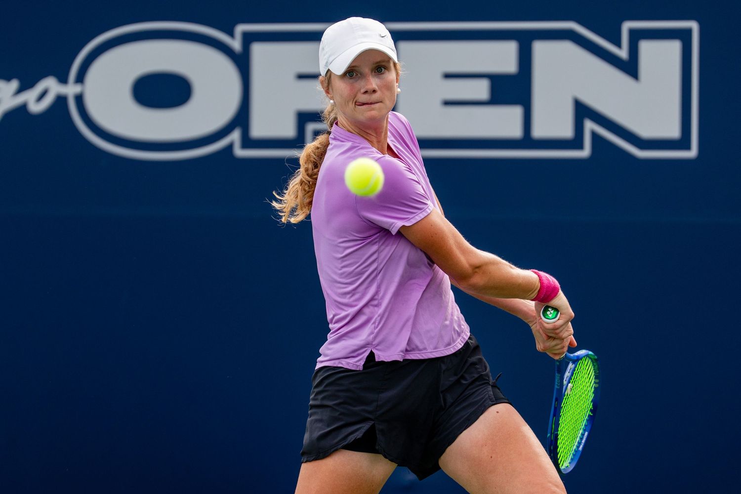 Female tennis player in purple shirt hits a backhand return at the San Diego Open tournament.