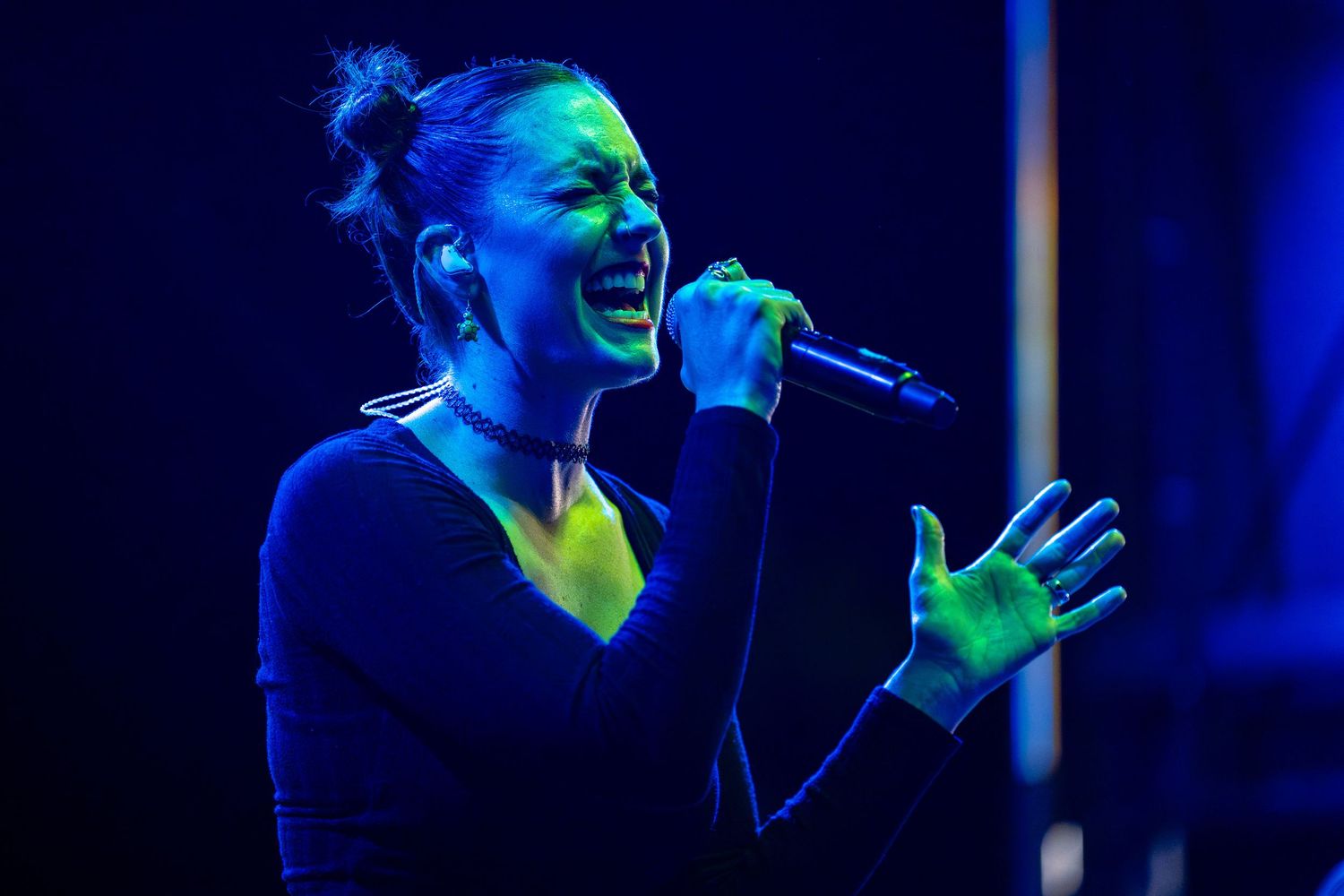 Female singer performing passionately on stage under dramatic blue and green stage lighting.