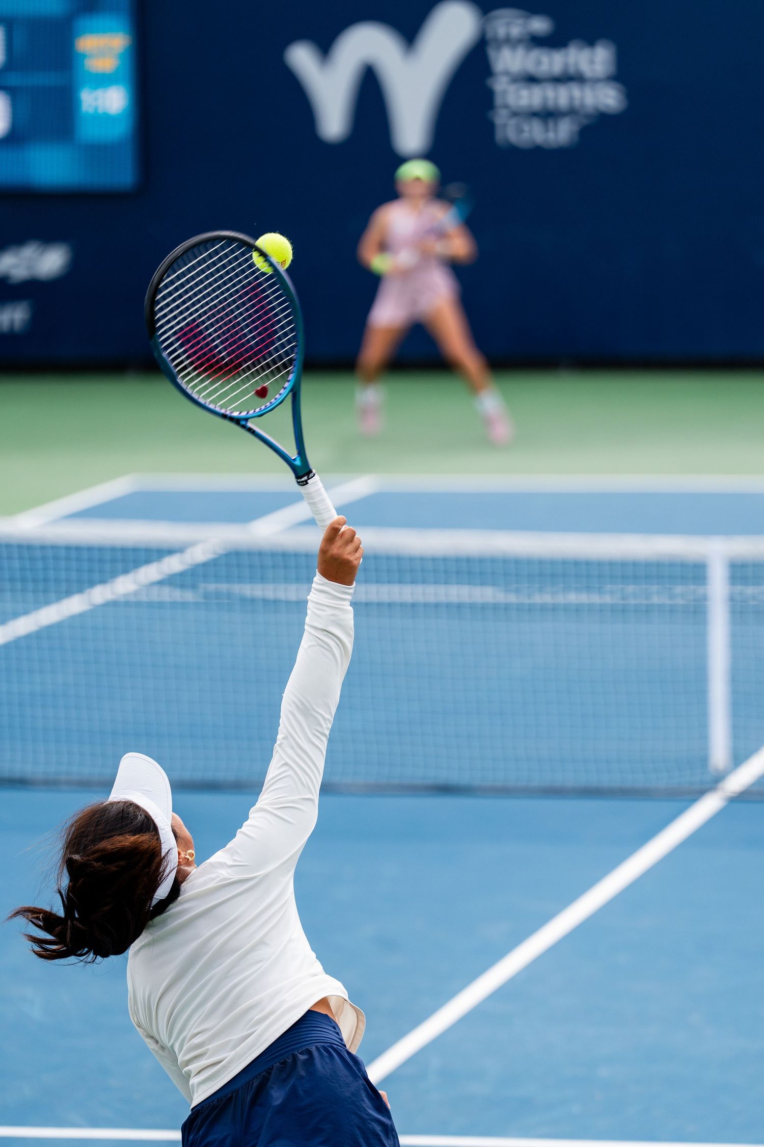 Female tennis player serves ball during World Tennis Tour match on blue hard court.