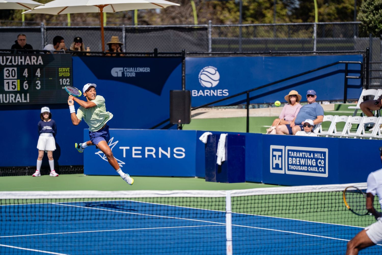 Tennis player leaps to return a shot during a Challenger Tour match on an outdoor hard court.