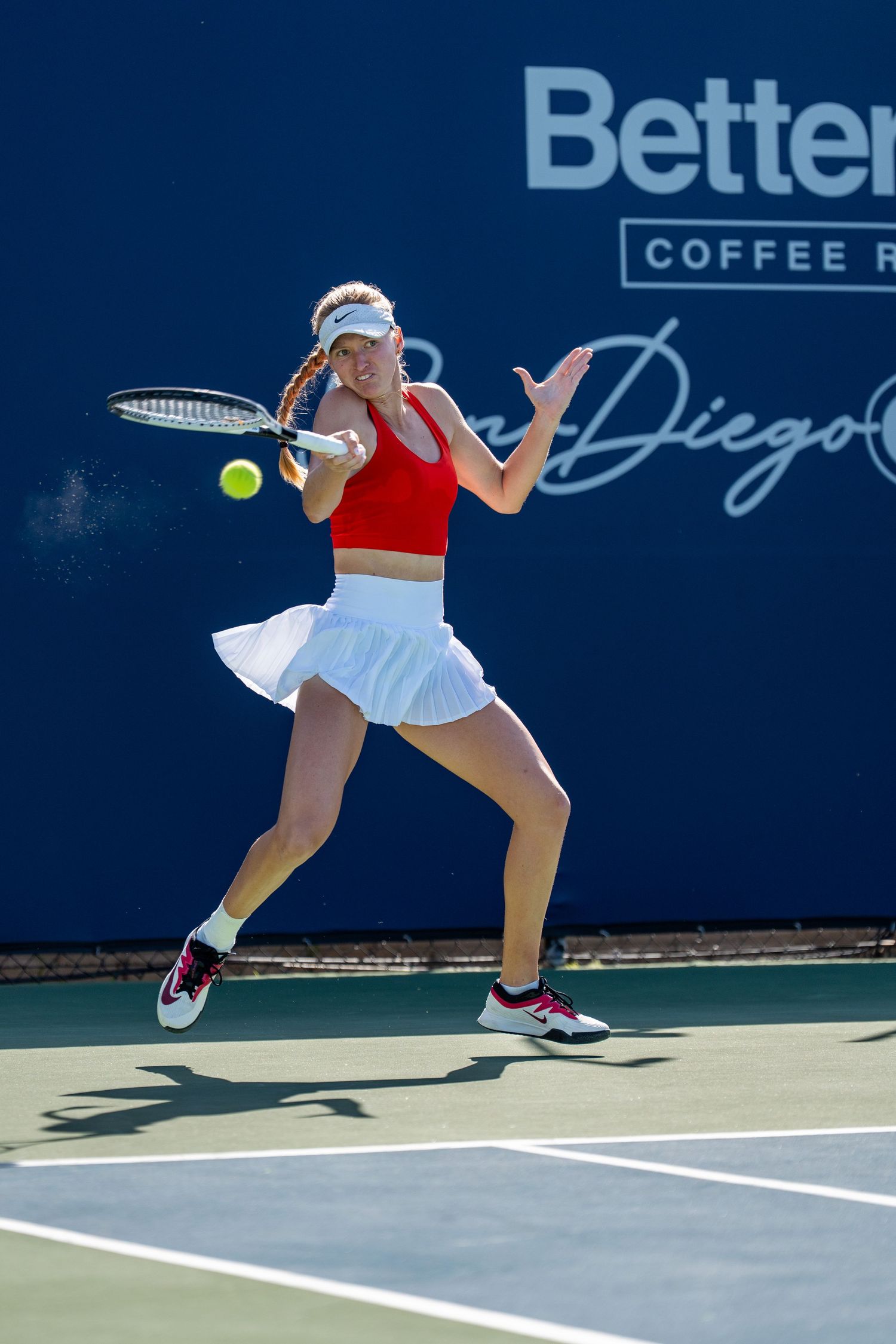 Young female tennis player in red top hits forehand at San Diego Open Better Buzz Coffee Roasters event.