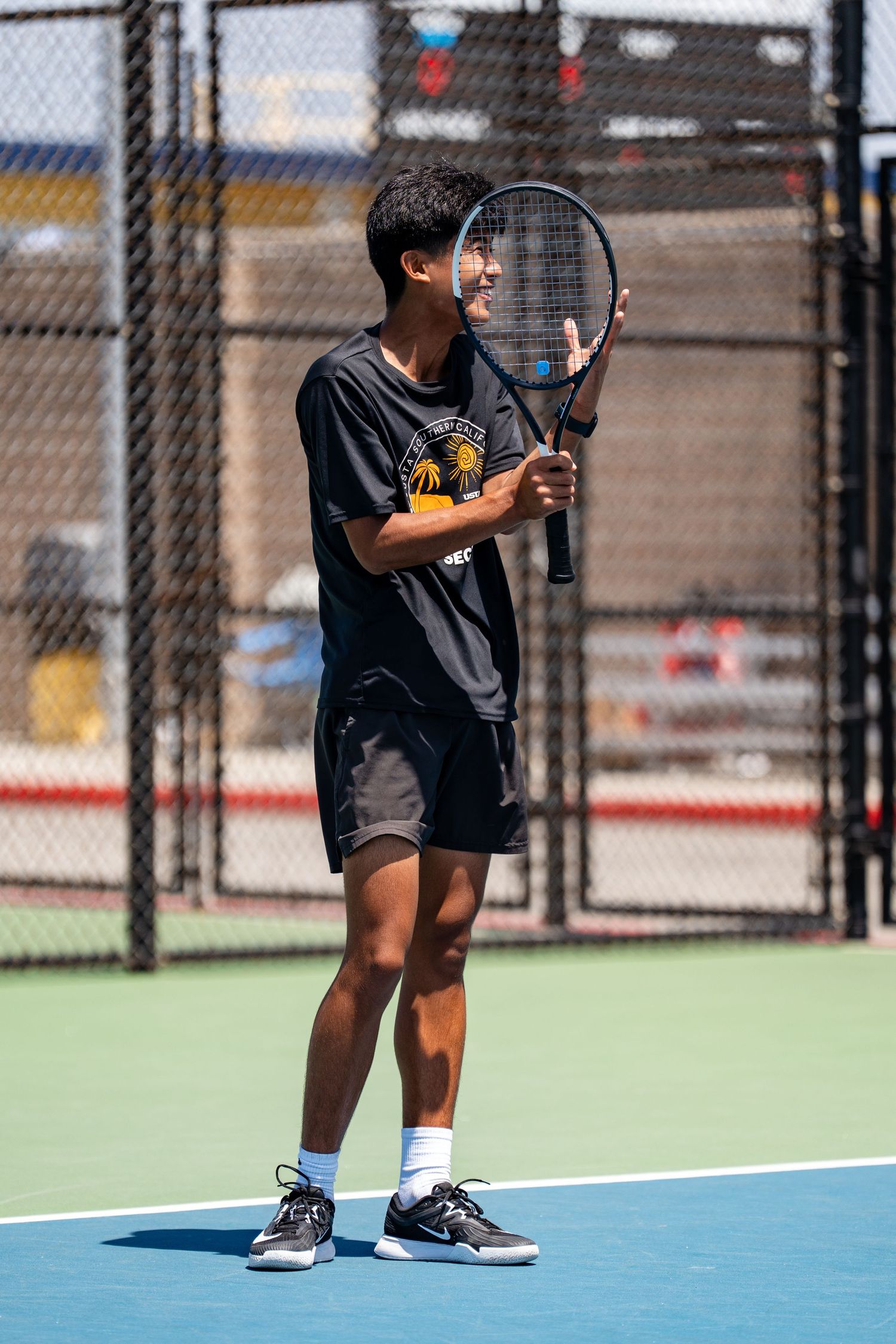 Smiling young male tennis player holds racket on a sunny outdoor blue tennis court.