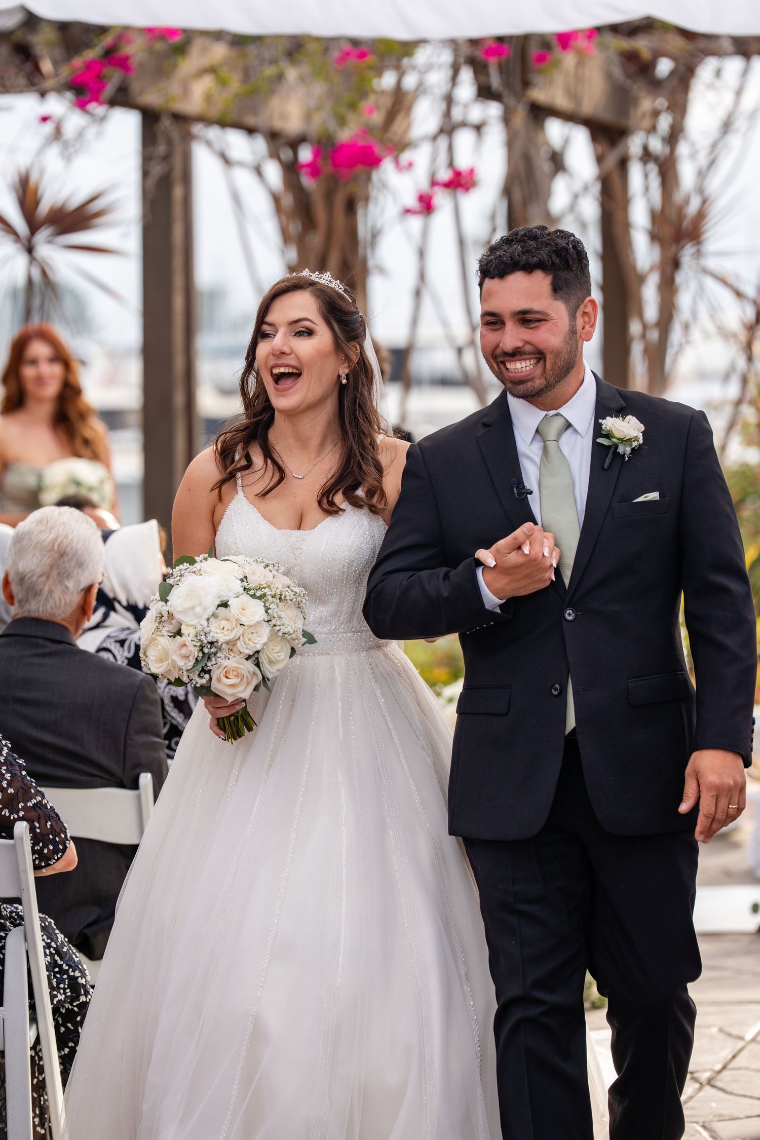 A joyful bride and groom walk down the aisle together at an outdoor wedding ceremony, smiling and holding hands.