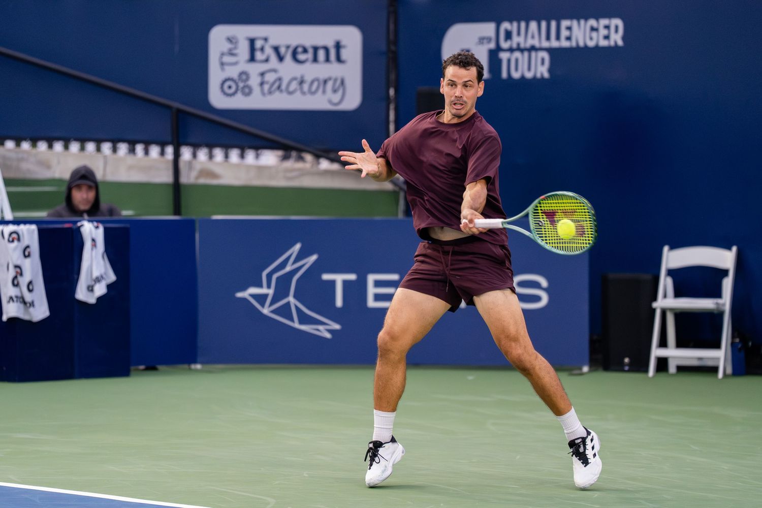 Tennis player in maroon outfit strikes a forehand during a Challenger Tour match at The Event Factory.