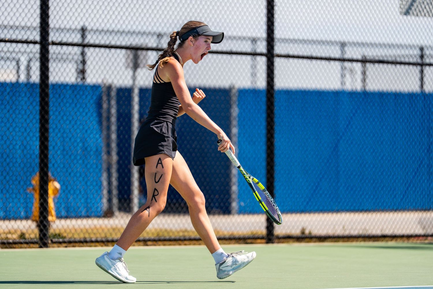 Female tennis player in black outfit walks confidently on an outdoor court holding her racket at her side.