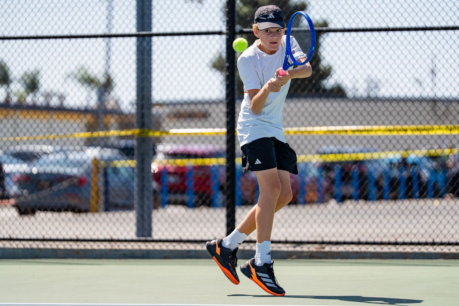 Male tennis player in white shirt lunges forward to hit a forehand on an outdoor court.
