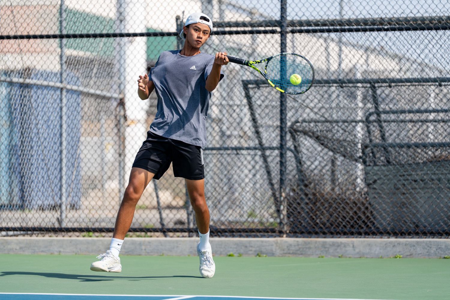 Young male tennis player in gray shirt and black shorts prepares to hit a forehand on an outdoor court.