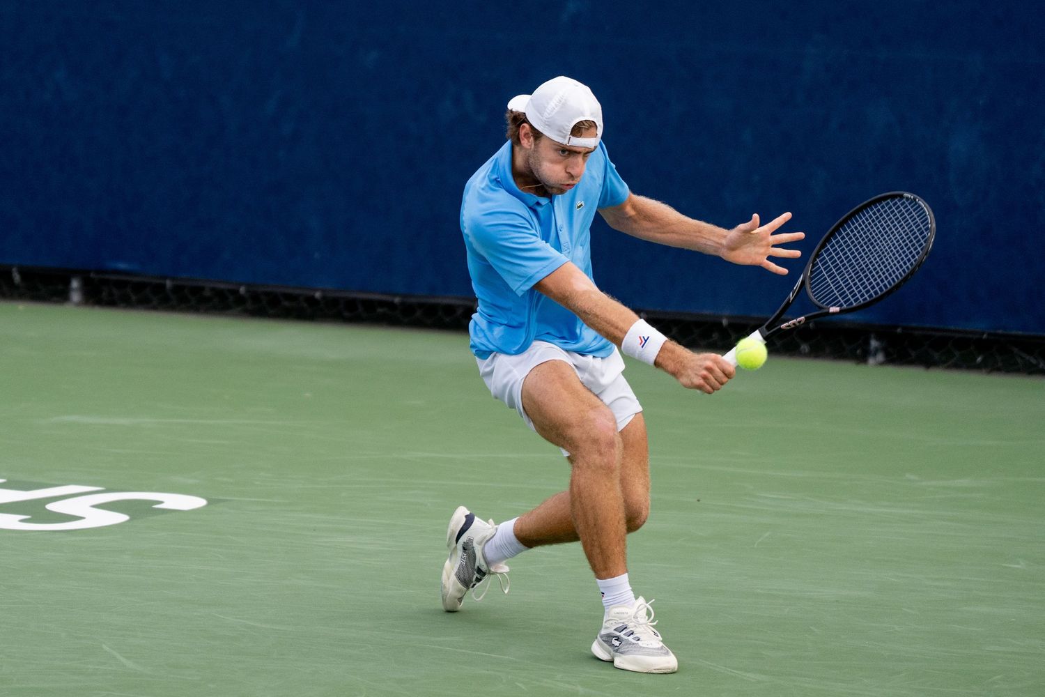 Tennis player in blue outfit hits a backhand shot on an outdoor hard court.