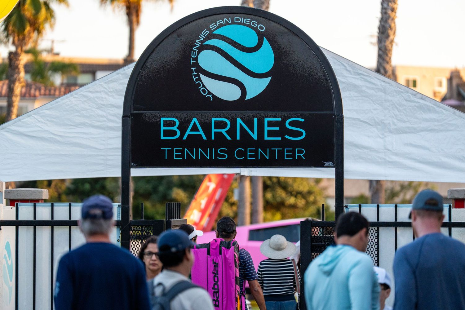 Spectators enter Barnes Tennis Center under illuminated arch sign at San Diego tennis tournament.