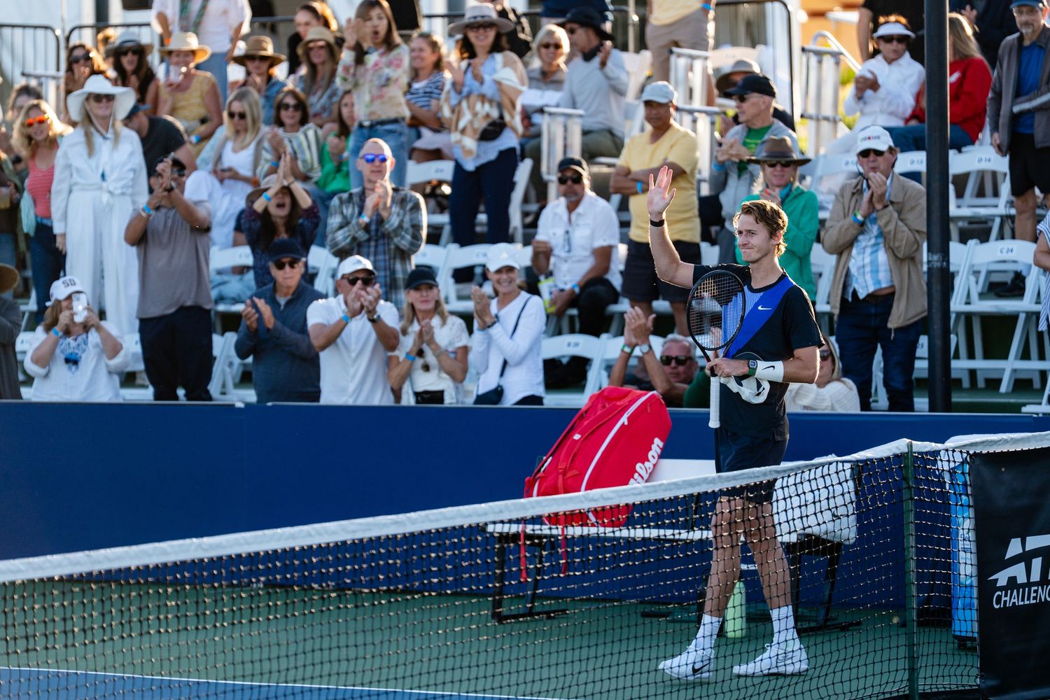 Tennis player acknowledges crowd at net during ATP tournament match with fans applauding in stands.