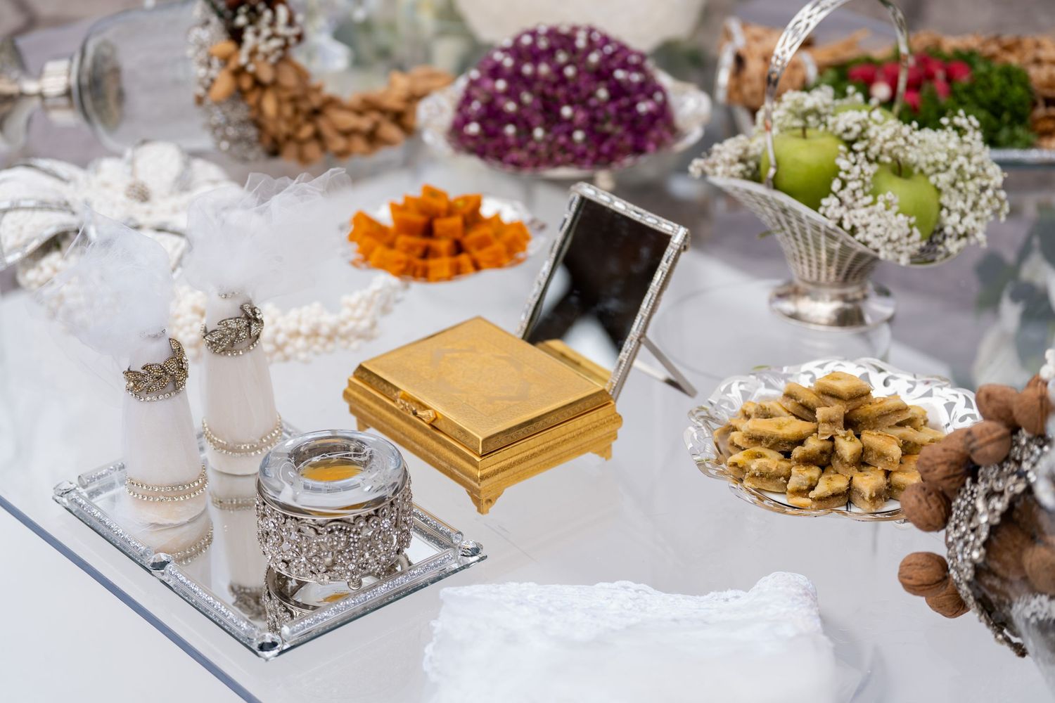 Elegant wedding sofreh aghd table with gold jewelry box, silver containers, dried fruits, nuts, and decorative items.