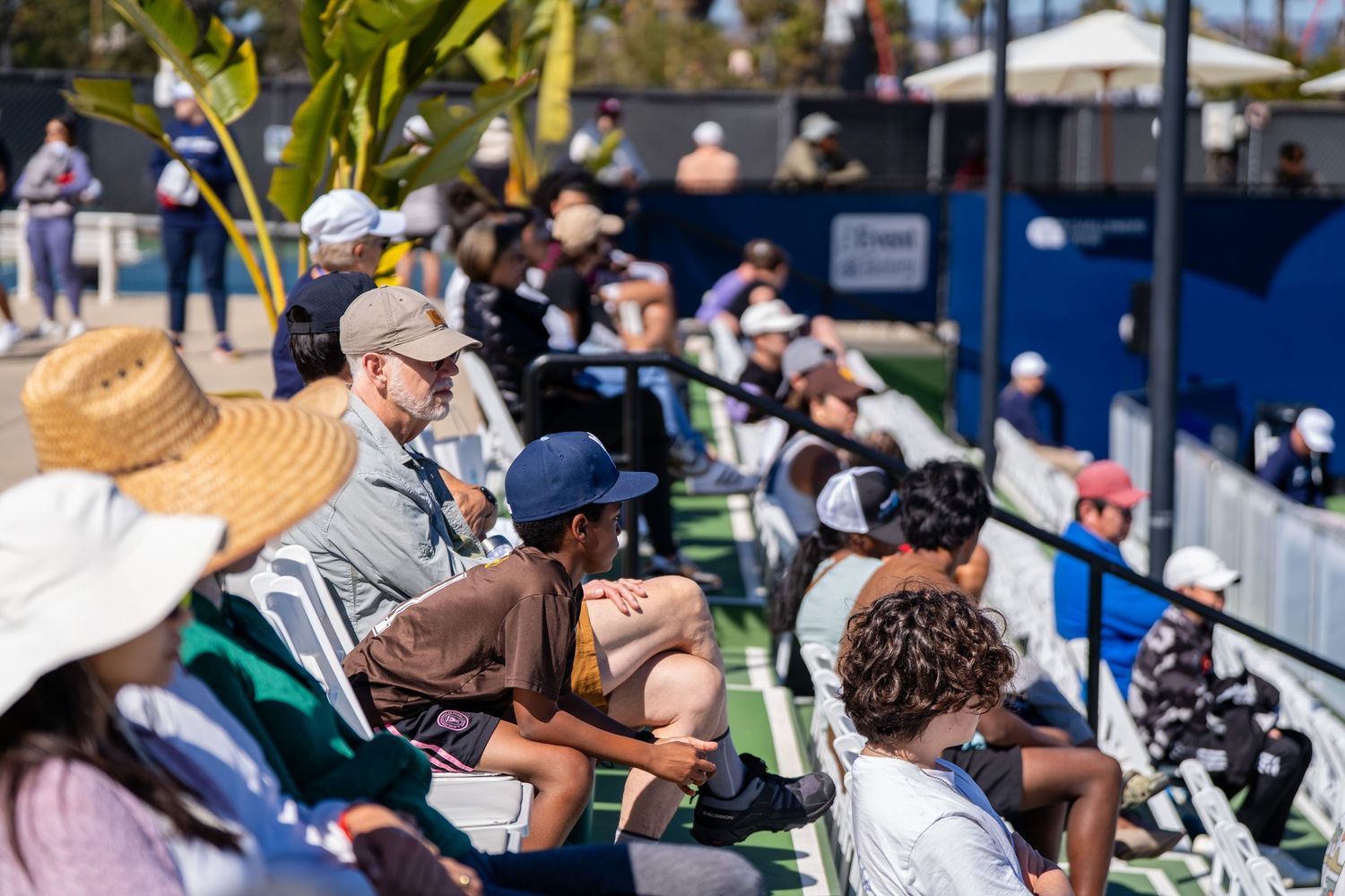 Diverse crowd of spectators watches tennis match at the San Diego Open.